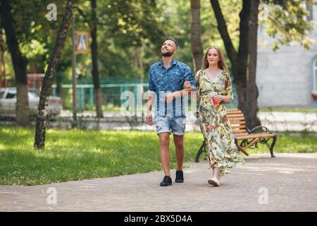 Bella giovane coppia in amore a piedi nel parco estivo con fredda limonata. Coppia romantica in un appuntamento all'aria aperta Foto Stock