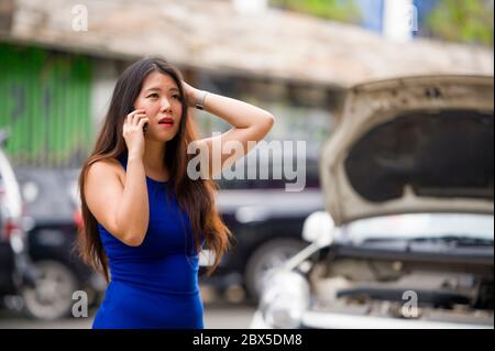 Giovane donna cinese asiatica disperata e sconvolta nello stress, si è bloccata sulla strada che soffre di un guasto al motore di auto che ha problemi meccanici a chiamare il cellulare phon Foto Stock