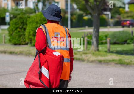 La British Royal Mail portalettere a piedi in una zona residenziale che trasportano un rosso sacchetta di lettere, per le consegne di mattina nel West Sussex, in Inghilterra, Regno Unito. Foto Stock