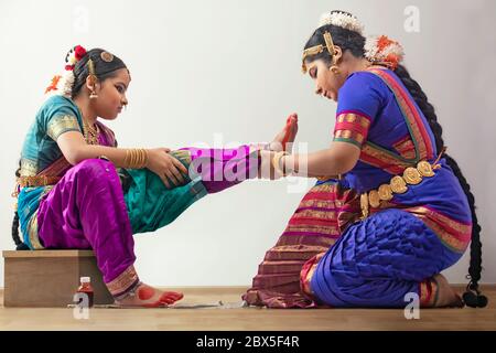Ballerina di Bharatnatyam che applica alta ai piedi del suo allievo. Foto Stock