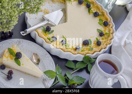 Cheesecake al limone fatto in casa in una teglia bianca in ceramica. Fetta di torta di limone su un piatto da portata bianco, tazza di tè bianco Foto Stock