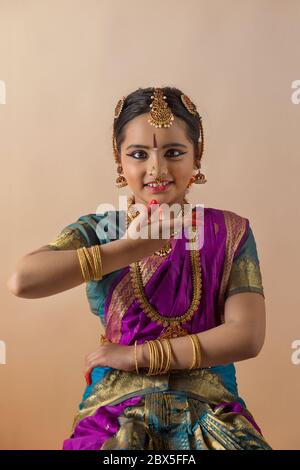 Giovane bharatnatyam ballerino in piedi con grazia davanti ad uno sfondo piano e sorridente. Foto Stock