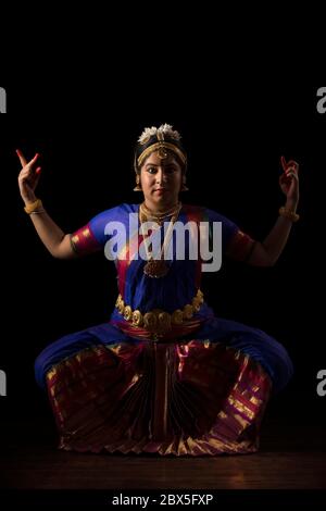 Ballerina di Bharatnatyam in una posa di devi durante la sua esecuzione su uno sfondo scuro. Foto Stock