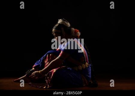 Ballerina di Bharatnatyam seduta e legando il ghungoo alle gambe. Foto Stock