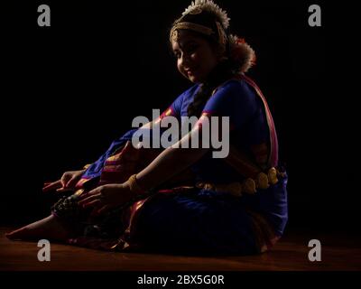 Ballerina di Bharatnatyam seduta e legando il ghungoo alle gambe. Foto Stock