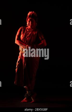 Ballerina Bharatnatyam in piedi con grazia davanti a uno sfondo scuro. Foto Stock