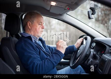 Uomo anziano che indossa gli occhiali prima di guidare, la sua vista non è buona, sicurezza e concetto di trasporto Foto Stock