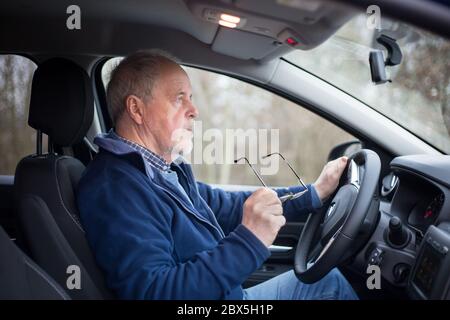 Uomo anziano che indossa gli occhiali prima di guidare, la sua vista non è buona, sicurezza e concetto di trasporto Foto Stock