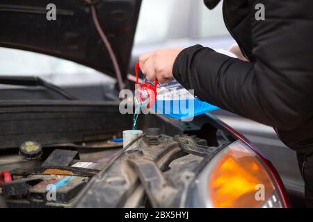 Dettaglio sul versamento di liquido antigelo per lavaggio in auto sporca da contenitore blu di acqua antigelo, concetto di auto Foto Stock