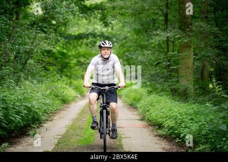 Uomo anziano in bicicletta durante l'estate bella in foresta, sorridente, godendo di viaggio, tempo libero Foto Stock