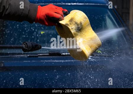 Pulizia auto con acqua ad alta pressione nel cortile posteriore. Pregando l'acqua sulla spugna gialla per pulire l'auto. Foto Stock