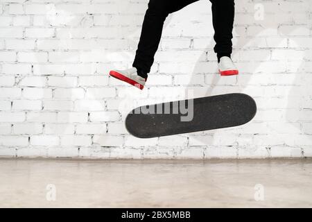 Skateboarder esecuzione skateboard trucco - kick flip su cemento. Atleta olimpico che pratica salto su sfondo bianco, preparazione per la concorrenza. Extr Foto Stock