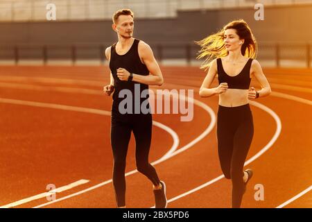Giovane uomo e donna che corre indossando abiti sportivi neri nello stadio moderno. Foto Stock