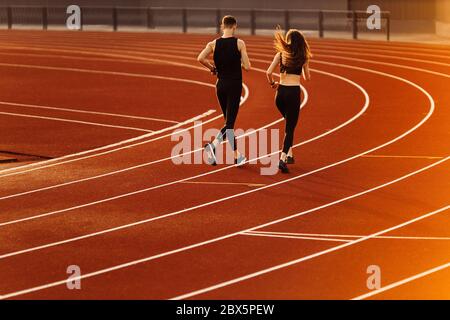 Giovane uomo e donna che corre su pista in stadio moderno. Foto Stock
