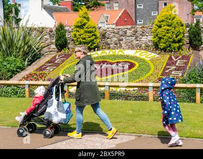 North Berwick, East Lothian, Scozia, Regno Unito, 5 giugno 2020. Tributo floreale e grazie al NHS in Lodge Gardens recentemente completato porta i visitatori ad ammirarlo sotto il sole. Una donna che spinge un bambino in un buggy cammina oltre con un bambino giovane Foto Stock