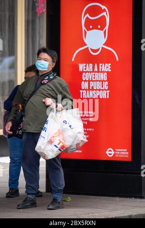 Un uomo che indossa una maschera protettiva per il viso attende presso una fermata dell'autobus nel centro di Londra, mostrando un avviso che consiglia ai passeggeri di indossare una copertura facciale sui mezzi pubblici, dopo l'annuncio che a partire da giugno 15 sarà obbligatorio indossare una copertura per il viso per i passeggeri dei mezzi di trasporto pubblici in Inghilterra. Foto Stock