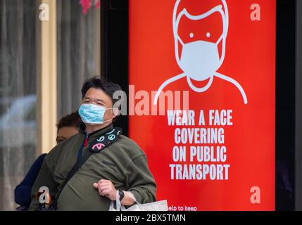 Un uomo che indossa una maschera protettiva per il viso attende presso una fermata dell'autobus nel centro di Londra, mostrando un avviso che consiglia ai passeggeri di indossare una copertura facciale sui mezzi pubblici, dopo l'annuncio che a partire da giugno 15 sarà obbligatorio indossare una copertura per il viso per i passeggeri dei mezzi di trasporto pubblici in Inghilterra. Foto Stock