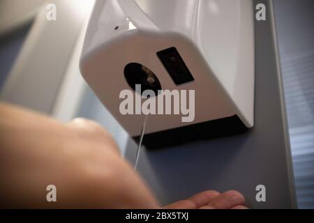 Mano maschile con dispenser automatico di alcol per la pulizia delle mani in ufficio o in ospedale per disinfettare virus e batteri - concetto di prevenzione delle infezioni Foto Stock