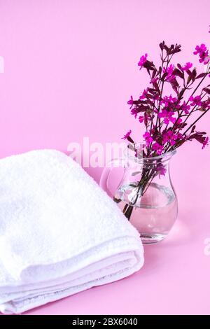 Asciugamani di cotone bianco puliti e freschi, trattamento Spa con ramo fiorito su sfondo rosa Foto Stock