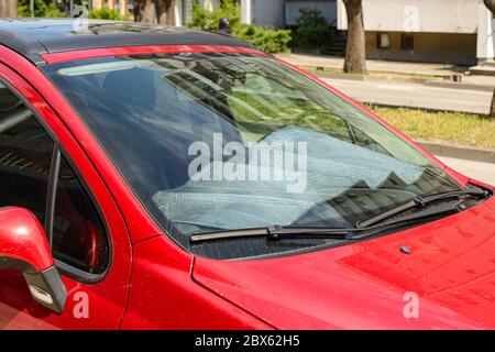 Le sfumature di sole in lamina copriva un pannello di un'auto rossa parcheggiata in strada in una soleggiata giornata estiva. Protezione solare riflettente realizzata in lamina metallica di argento contro i raggi uv Foto Stock