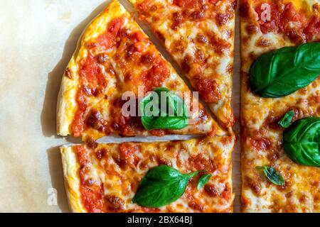 Vista dall'alto della gustosa pizza margarita italiana calda e cotta a fette su carta da forno appena prelevata dal forno. Mozzarella fusa, pomodoro Foto Stock