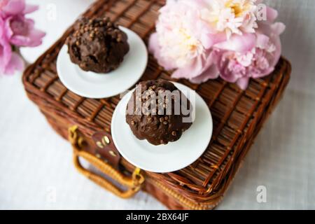 Muffin al cioccolato e di un bel colore rosa peonie giacciono su una valigia di legno. Bella composizione. Foto Stock