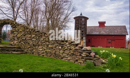 una vista attraverso un arco di pietra di silo rotondo storico restaurato e fienile rosso in primavera Foto Stock