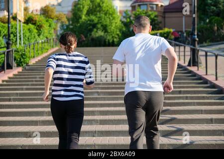 Coppia che corre sulle scale nella vista posteriore della città Foto Stock