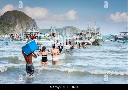Turisti e le mani locali della barca filippina si sfilano o portano rifornimenti alle numerose barche ormeggiate nel surf in attesa di visitare le isole e le spiagge. Foto Stock