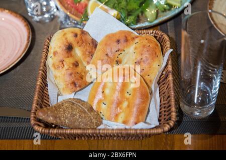 Angolo di Alta Vista di una varietà di pane appena sfornato nel cesto di vimini sfondo di legno . Cestino del pane su un tavolo di legno. Composizione con varietà di Foto Stock