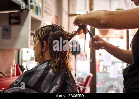Un primo piano di un parrucchiere che taglia i capelli del cliente. Piccola impresa Foto Stock