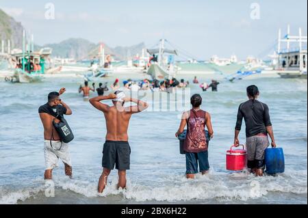 Turisti e le mani locali della barca filippina si sfilano o portano rifornimenti alle numerose barche ormeggiate nel surf in attesa di visitare le isole e le spiagge. Foto Stock