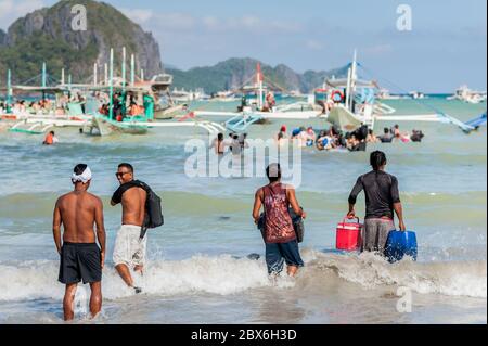 Turisti e le mani locali della barca filippina si sfilano o portano rifornimenti alle numerose barche ormeggiate nel surf in attesa di visitare le isole e le spiagge. Foto Stock