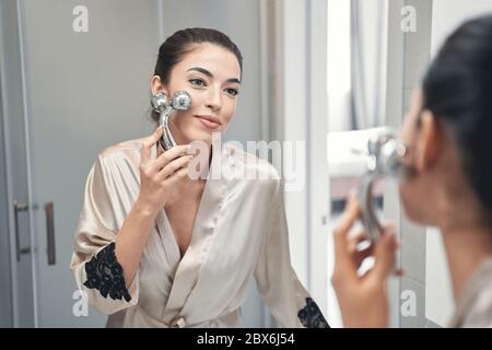 Piacevole giovane donna bella-osservante che si prende cura della sua pelle alla mattina Foto Stock