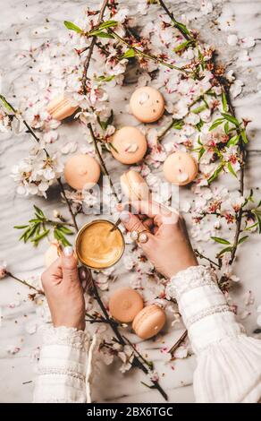 Mani donne che tengono il caffè fresco sopra i biscotti e fiori di macaron Foto Stock