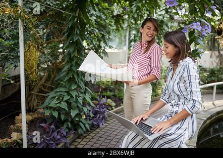 due architetti di paesaggio femminili che hanno, divertimento, godendosi, ridendo e sorridendo mentre fanno i programmi per la nuova disposizione per il giardino botanico, tenendo il pape Foto Stock