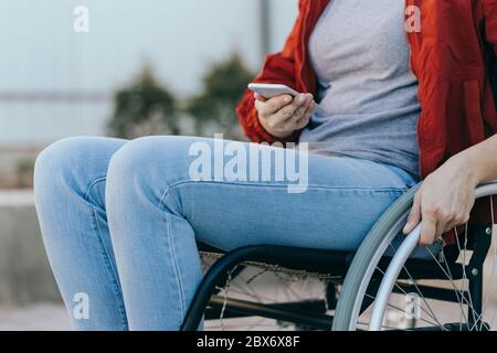 Una donna in sedia a rotelle con un telefono in mano cammina per strada, la sua mano è vicina, un irriconoscibile Foto Stock