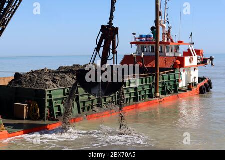 Grande gru galleggiante industriale che scarica sabbia, pulendo la sabbia rossa nave sulla spiaggia di Riminy, Italia in giornata di sole luminoso Foto Stock