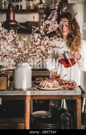 Giovane donna che versa il tè sul tavolo con la torta di primavera Foto Stock