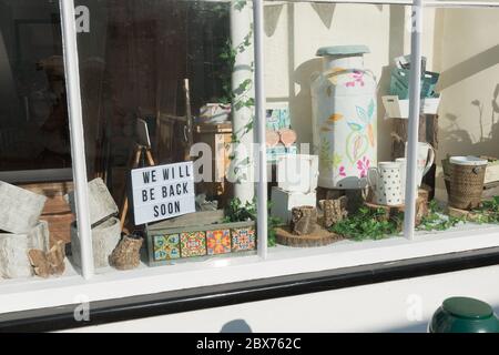 Vista della vetrina con articoli assortiti in esposizione e il cartello con la scritta "We will be back soon". Il negozio è temporaneamente libero durante il blocco COVID-19. Foto Stock