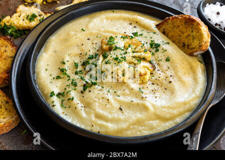 Zuppa di cavolfiore arrosto in ciotola nera rustica, con toast croccante e di pasta acida. Foto Stock