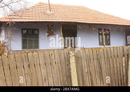 Casa tradizionale a un piano nella Contea di Teleorman, Romania. Proprietà recintata. Casa di fango con facciata danneggiata. Foto Stock