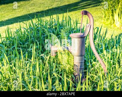 Vecchio standpipe acqua arrugginito in piedi in erba alta nel giardino svedese. Decorazione vintage per casa di campagna. Costruzione di pompaggio manuale. Va Foto Stock