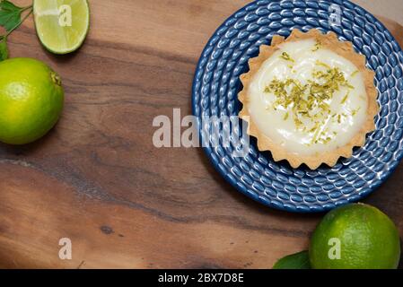 Vista dall'alto della tradizionale torta francese al limone su legno. Vista delle sezioni del limone dall'alto. Tartlet su piatto blu d'annata e fette di limone su tavola di legno. Foto Stock
