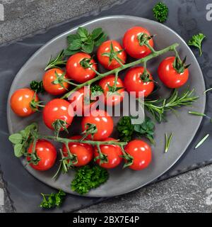 Pomodori ciliegini sulla vite con erbe fresche. Vista dall'alto su ardesia. Foto Stock