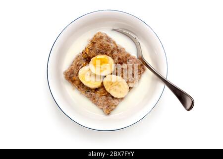 Ciotola di cereali per la colazione con cucchiaio. Vista dall'alto, isolata su bianco. Biscotti di grano conditi con banana e miele. Foto Stock