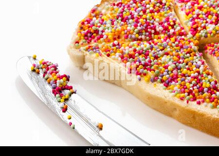 Pane fata con coltello per burro, vista laterale. Cibo tradizionale australiano per i bambini, centinaia e migliaia di caramelle spruzzano sul pane bianco. Foto Stock