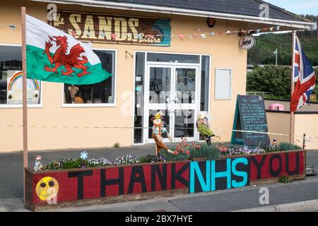 Bandiera gallese, e, Union Jack, bandiera con NHS grazie,Servizio sanitario Nazionale,supporto,poster,banner,di,supporto,pubblico,esterno,chiuso,Sands,cafe,ristorante,che,è,chiuso,a causa,Coronavirus,Covid 19,pandemic,in,Borth,mare,vacanza,resort,nord,di,Aberystwyth,Cereturismo occidentale ha attualmente aperto 5 miglia di viaggi, Galles e Galles.un numero di anziani.la politica di viaggi in Galles, non è aperto di vita, e Galles.un numero di persone anziana, è di persone anziana, non è di vita, ha aperto di vita, e di vita in Galles.un numero di persone anziana, è di vita in Galles.un numero di persone anziana, è di persone anziana, ha ma ha anche un'economia con molti che dipendono dal turismo, turisti. Foto Stock