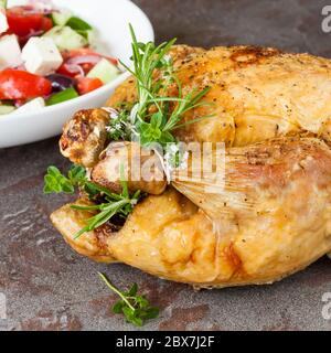 Pollo arrosto con erbe fresche e insalata greca alle spalle. Foto Stock
