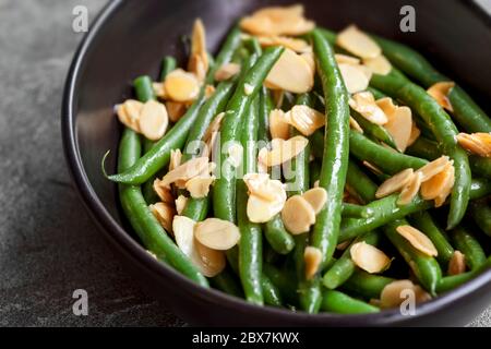 Fagioli verdi con mandorle tostate, in ciotola nera su ardesia scura. Foto Stock